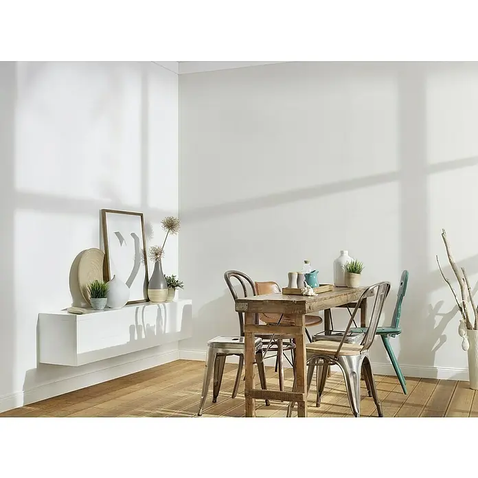 A.S. Création Trendwall 2 Vliestapete - Reinweiß, Uni, 10,05 x 0,53 m - Einrichtungsidee mit einem Holztisch, Stühlen in verschiedenen Designs und einer weißen Wandkonsole mit Dekoration.