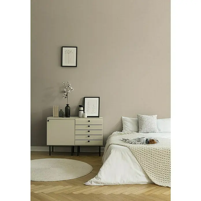 A.S. Création Titanium 3 Vliestapete - Pastelles Beige, Uni, 10,05 x 0,53 m - Ein helles Schlafzimmer mit einem hellen Nachttisch mit Schubladen, einem runden Teppich und einem gemütlichen Bett mit Decke.