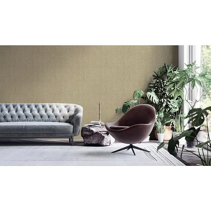 A.S. Création Hygge 2 Vliestapete Bambusstruktur - Taupe, Uni, 10,05 x 0,53 m - Ein Wohnzimmer mit einem grauen Sofa, einem braunen Sessel und vielen Pflanzen.
