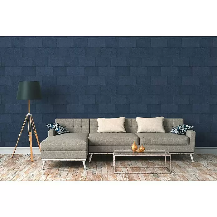 A.S. Création Titanium 3 Vliestapete - Blau, Steinoptik, 10,05 x 0,53 m - Ein modernes Wohnzimmer mit grauem Ecksofa, Glastisch und Dreibein-Stehlampe vor einer blauen Strukturwand.