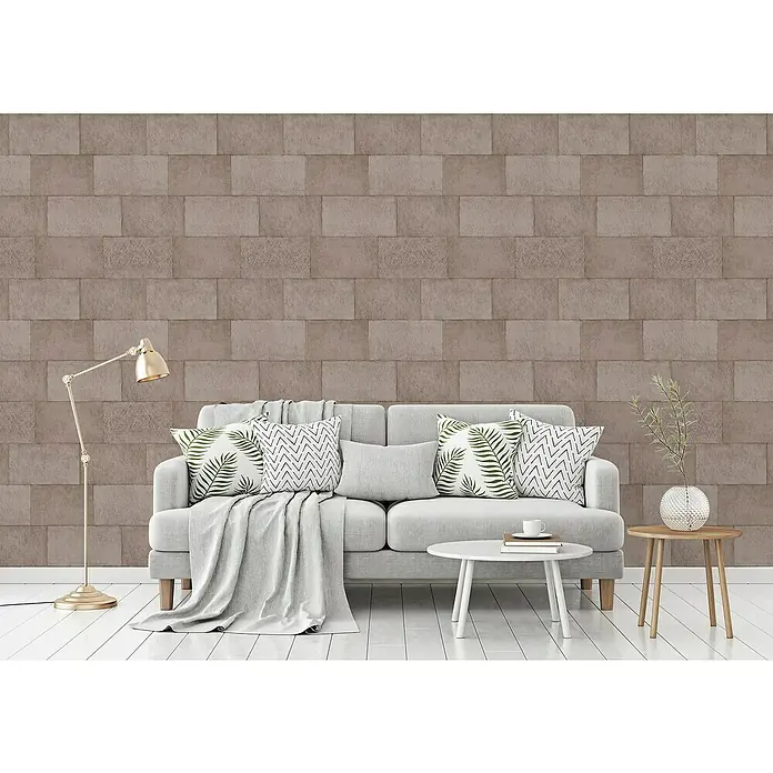 A.S. Création Titanium 3 Vliestapete - Braun, Steinoptik, 10,05 x 0,53 m - Einladender Wohnraum mit einem grauen Sofa, Zierkissen und einem stilvollen Hintergrund mit Mauerwerk-Tapete für eine moderne Atmosphäre.