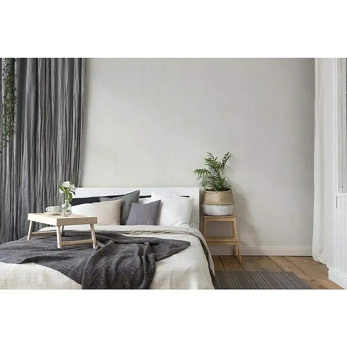 A.S. Création Titanium 3 Vliestapete - Pastellweiß, Uni, 10,05 x 0,53 m - Einladendes Schlafzimmer mit einem Bett mit Frühstückstablett, Pflanzen auf einem Nachttisch und sanften grauen Vorhängen, die eine friedliche Atmosphäre schaffen.