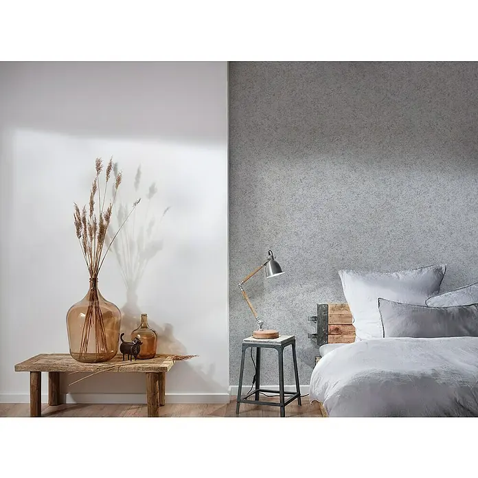 A.S. Création Attractive Vliestapete - Grau/Silber, Uni, 10,05 x 0,53 m - Stilvolles Interieur mit einer großen Glasvase auf einem Holztisch, ergänzt durch eine moderne Lampe und ein gemütliches Bett im Hintergrund.