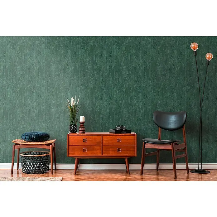A.S. Création Trendwall 2 Vliestapete Rostoptik - Rost/Grün, Metalloptik, 10,05 x 0,53 m - Wohnzimmer-Interieur mit einem dunklen Holzschrank, einem Stuhl und einer Stehlampe vor einer grünen Wand.
