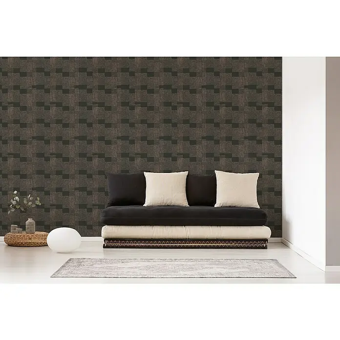 A.S. Création Desert Lodge Vliestapete Ethno-Muster - Kupfer/Schwarz, Grafisch, 10,05 x 0,53 m - Nahaufnahme eines stilvollen Futons mit Kissen, platziert vor einer gemusterten Wand, der eine moderne und gemütliche Atmosphäre ausstrahlt.