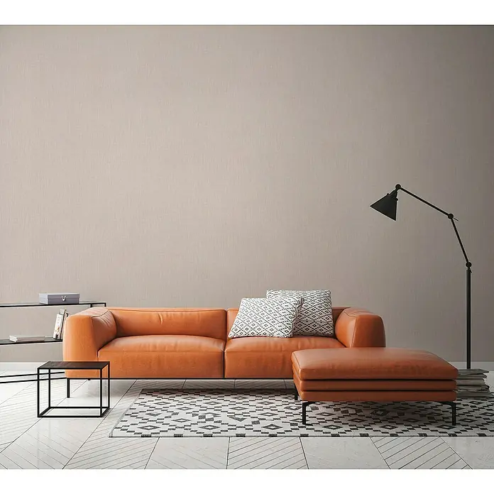 A.S. Création Daniel Hechter 6 Vliestapete Textilstruktur - Hellbeige, Uni, 10,05 x 0,53 m - Ein modernes Wohnzimmer mit einem orangefarbenen Ledersofa, einem passenden Ottomanen und einem schwarzen Bücherregal mit Beistelltisch.