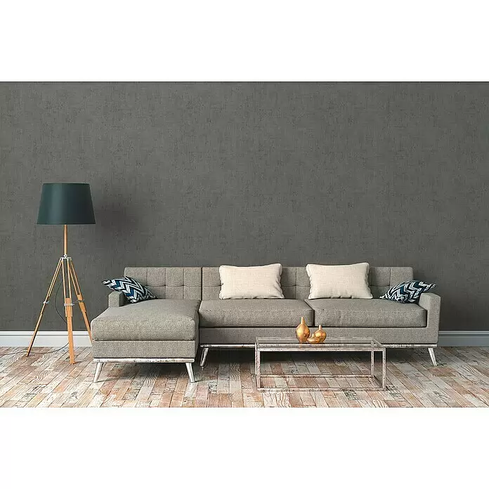 A.S. Création Cuba Vliestapete - Grau, Uni, 10,05 x 0,53 m - Ein graues Ecksofa mit hellen Kissen und gemusterten Zierkissen in einem modernen Wohnzimmer.