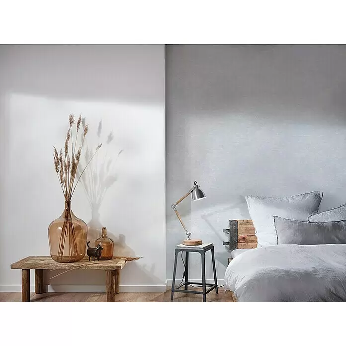 A.S. Création Attractive Vliestapete - Pastelles Beige-Weiß, Uni, 10,05 x 0,53 m - Schlafzimmerszene: industrielle Schreibtischlampe auf einem Hocker am Bett, rustikaler Konsolentisch mit bernsteinfarbener Glasvase und Trockenpflanzen.