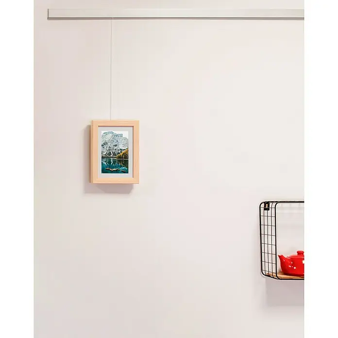Nielsen Holzrahmen Apollo - 13 x 18 cm, Natur - Ein gerahmtes Landschaftsbild mit Bergen hängt an einer weißen Wand unter einem Hängesystem. Eine Drahtregal mit Teekanne ist rechts zu sehen.
