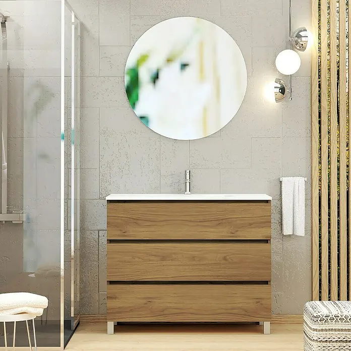 Artysan Conjunto de mueble de baño Basic 3C - Ancho: 100 cm, Ancho total del mueble de baño: 100 cm, Roble waira, 3 pzs. - Mueble de baño con cajones de madera y encimera blanca, ubicado debajo de un espejo redondo y al lado de una ducha de vidrio.