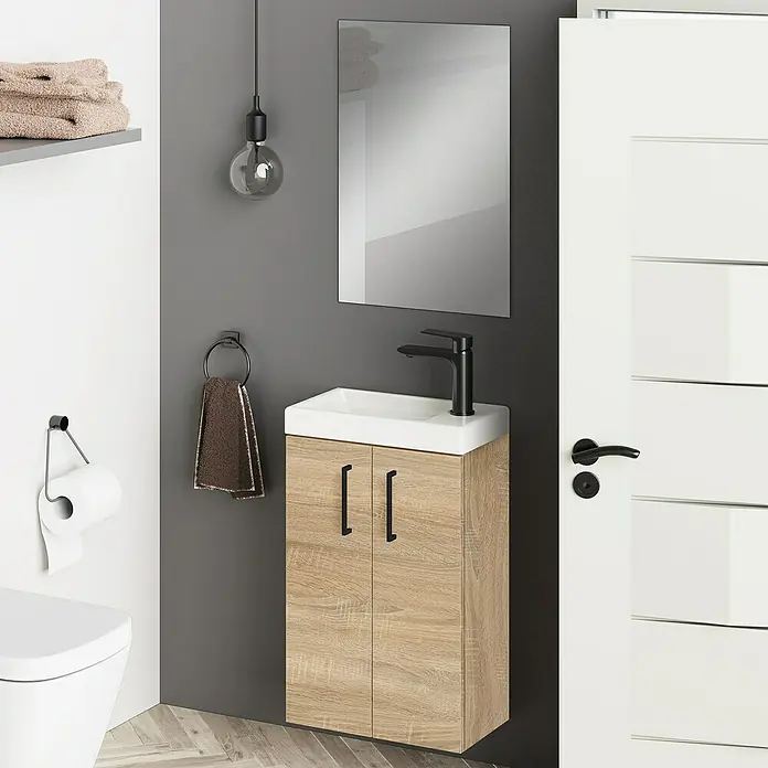 Artysan Conjunto de mueble de baño Super Mini - Natural, 3 pzs. - Un mueble de baño con un gabinete con textura de madera y un grifo negro debajo de un espejo y una bombilla.