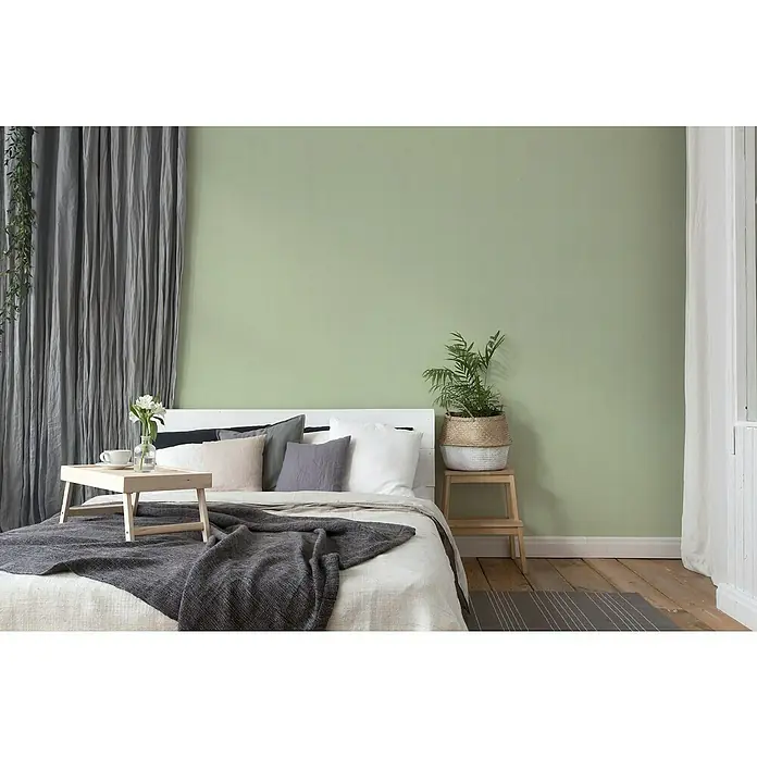 A.S. Création Attractive Vliestapete - Ambientegrün, Uni, 10,05 x 0,53 m - Schlafzimmer mit einem Bett und einem kleinen Holztisch darauf, neben einem grünen Wandhintergrund.