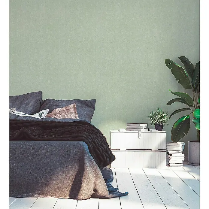 A.S. Création Hygge 2 Vliestapete - Grün/Schwarz, Uni, 10,05 x 0,53 m - Schlafzimmer-Interieur mit einem gemütlichen Bett mit grauer Bettwäsche, einem Nachttisch und Zimmerpflanzen. Das Zimmer hat eine ruhige Atmosphäre.