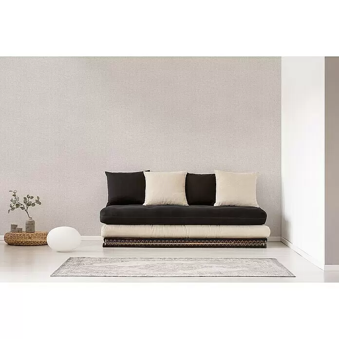 A.S. Création Desert Lodge Vliestapete - Creme, Uni, 10,05 x 0,53 m, Feine Struktur - Niedriges Sofa aus schwarzen und beigen gestapelten Kissen und Polstern.