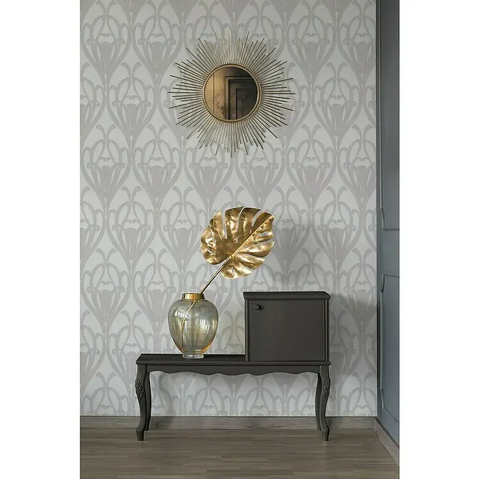 A.S. Création Mata Hari Vliestapete Barock - Grau/Weiß, Ornament, 10,05 x 0,53 m - Ein dekoratives Arrangement mit einem grauen Tisch, einer goldenen Blattdeko, einem Spiegel und einer Kommode vor einer gemusterten Tapete.