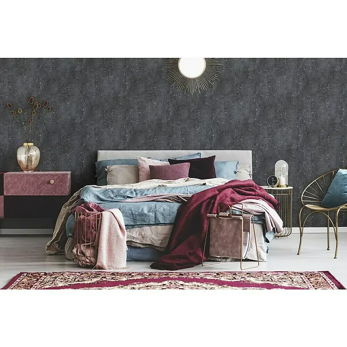 A.S. Création Titanium 3 Vliestapete I - Schwarz, Betonoptik, 10,05 x 0,53 m - Schlafzimmer mit Doppelbett, Nachttisch und goldfarbenem Stuhl. Das Zimmer ist in dunklen Farben gehalten und mit Textilien dekoriert.