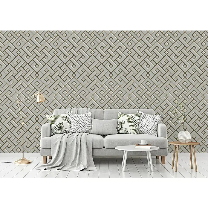 A.S. Création Michalsky 4 Vliestapete Meander - Grau/Gold, 3D-Optik, 10,05 x 0,53 m - Ein stilvolles Wohnzimmer mit einem modernen grauen Sofa, Kissen und einem goldenen Stehlampe vor einer geometrischen Tapete.