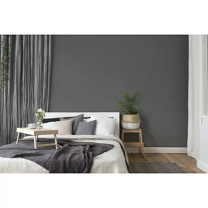 A.S. Création Desert Lodge Vliestapete - Eisengrau, Uni, 10,05 x 0,53 m - Schlafzimmer mit weißer/grauer Bettwäsche, dunkelgrauer Strickdecke und einem Frühstückstablett aus Holz mit Blumen.
