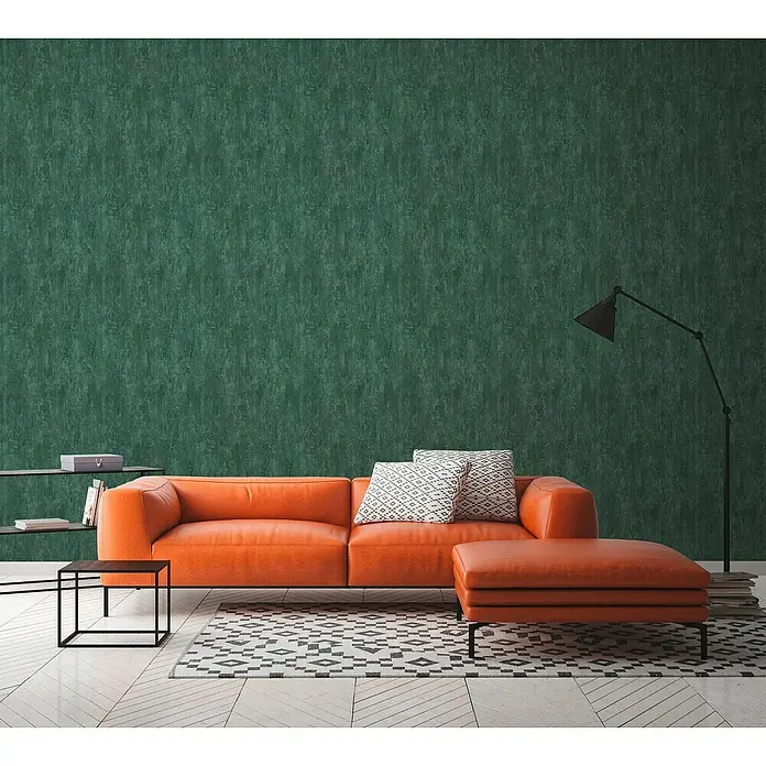 A.S. Création Trendwall 2 Vliestapete Rostoptik - Rost/Grün, Metalloptik, 10,05 x 0,53 m - Wohnzimmer-Szene mit einem modernen orangefarbenen Ledersofa mit Ottomane, gemusterten Kissen und einem minimalistischen Beistelltisch.