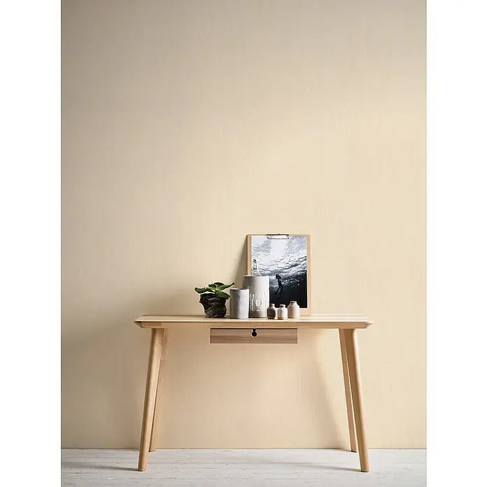 A.S. Création Hygge 2 Vliestapete Gewebestruktur - Beige, Uni, 10,05 x 0,53 m - Ein heller Holzschreibtisch mit einer Schublade und einigen Dekorationsgegenständen.