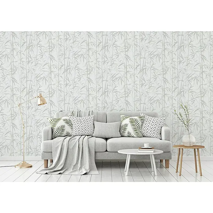 A.S. Création Michalsky 4 Vliestapete Bambus - Beige/Creme, Floral, 10,05 x 0,53 m - Ein Wohnzimmer mit einem grauen Sofa, Kissen mit Pflanzenmotiven, einem goldenen Stehlampe und einer Tapete mit Bambusmuster.