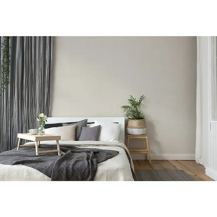 A.S. Création Hygge 2 Vliestapete Gewebe - Rosè, Uni, 10,05 x 0,53 m - Einladendes Schlafzimmer mit Bett, Tagesdecke, Kissen, Beistelltisch mit Pflanze und Frühstückstablett vor grauem Vorhang.