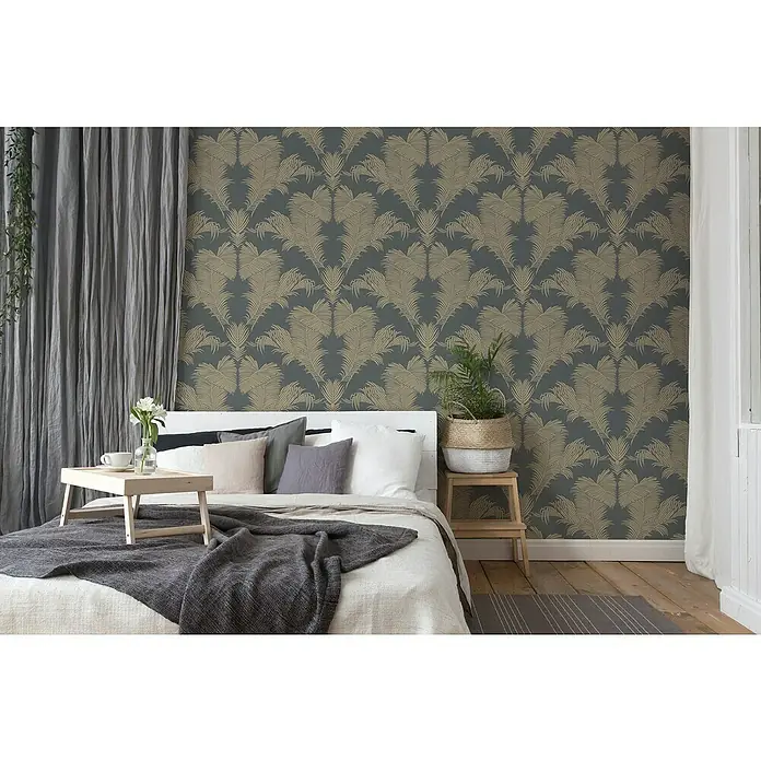 A.S. Création Trendwall 2 Vliestapete Palmen-Ornament - Grau/Gold, Floral, 10,05 x 0,53 m - Schlafzimmer mit einem Bett, das mit Kissen und einer Decke dekoriert ist, und einer Nachttischlampe mit einer Pflanze darauf.