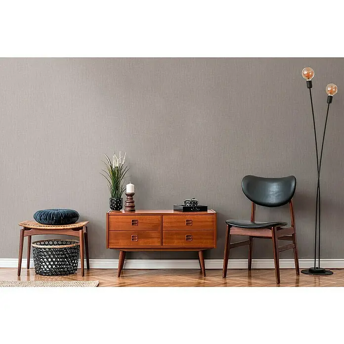 A.S. Création Daniel Hechter 6 Vliestapete Textilstruktur - Beige, Uni, 10,05 x 0,53 m - Gemütliches Interieur mit einer Kommode aus Holz, einem Stuhl und einer Stehlampe, die ein warmes Ambiente erzeugen. Perfekt für Wohnräume.