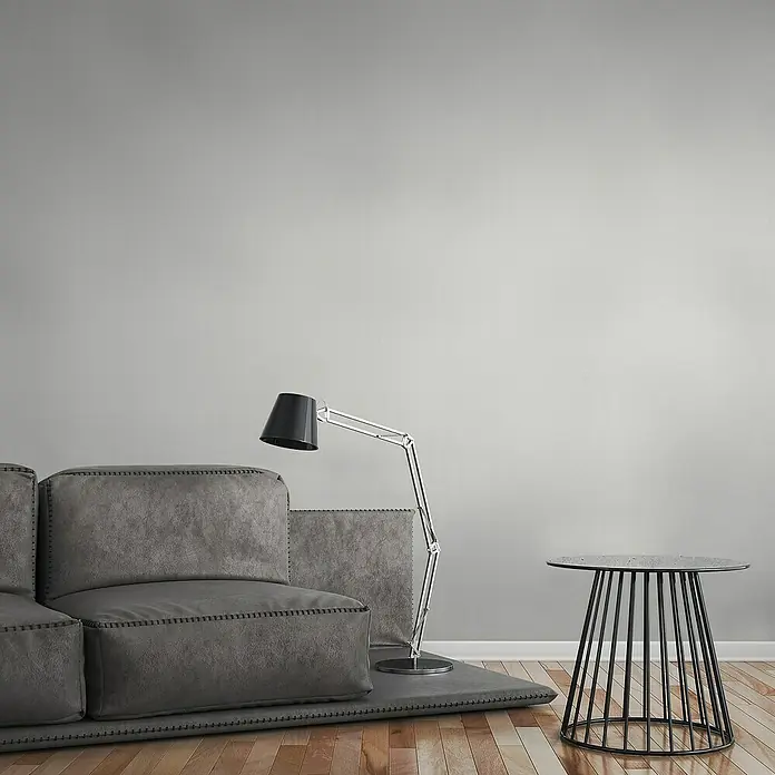A.S. Création Attractive Vliestapete - Hellweiß, Uni, 10,05 x 0,53 m - Das Bild zeigt ein modernes Wohnzimmer mit einem grauen Sofa, einer Stehlampe und einem Beistelltisch. Die Einrichtung ist minimalistisch und stilvoll.