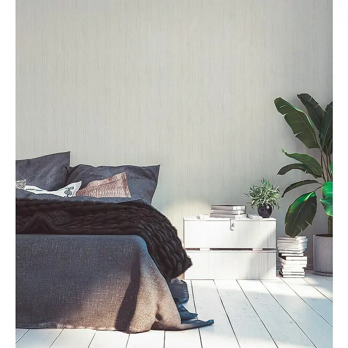A.S. Création Hygge 2 Vliestapete Bäume - Creme/Beige, Floral, 10,05 x 0,53 m - Schlafzimmerinterieur mit Bett, Nachttisch, Büchern und einer Topfpflanze, das eine gemütliche und entspannende Atmosphäre schafft.