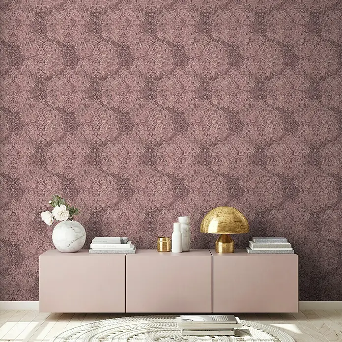 A.S. Création Mata Hari Vliestapete Barock antik - Rosa/Rot, Ornament, 10,05 x 0,53 m - Einrichten mit Stil: Kommode in sanftem Rosa, dekoriert mit Büchern, Kerzen und einer goldenen Lampe, vor einer Wand mit floralem Muster.