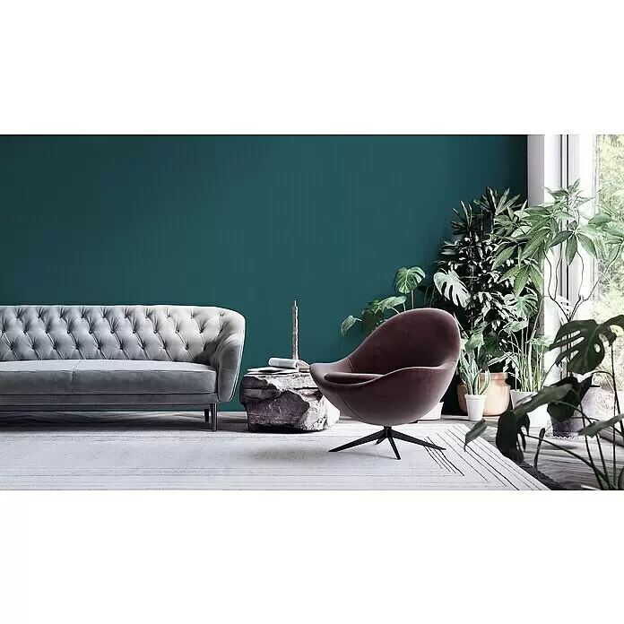A.S. Création My Home My Spa Vliestapete Textstruktur I - Petrol, Uni, 10,05 x 0,53 m - Wohnzimmer mit grauem getuftetem Sofa, braunem Sessel, Steintisch und Pflanzen vor einer tealfarbenen Wand.