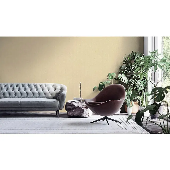 A.S. Création Hygge 2 Vliestapete Gewebe - Beige, Uni, 10,05 x 0,53 m - Elegantes Wohnzimmer mit grauem Sofa, braunem Sessel und einer Auswahl an Zimmerpflanzen für eine gemütliche Atmosphäre.