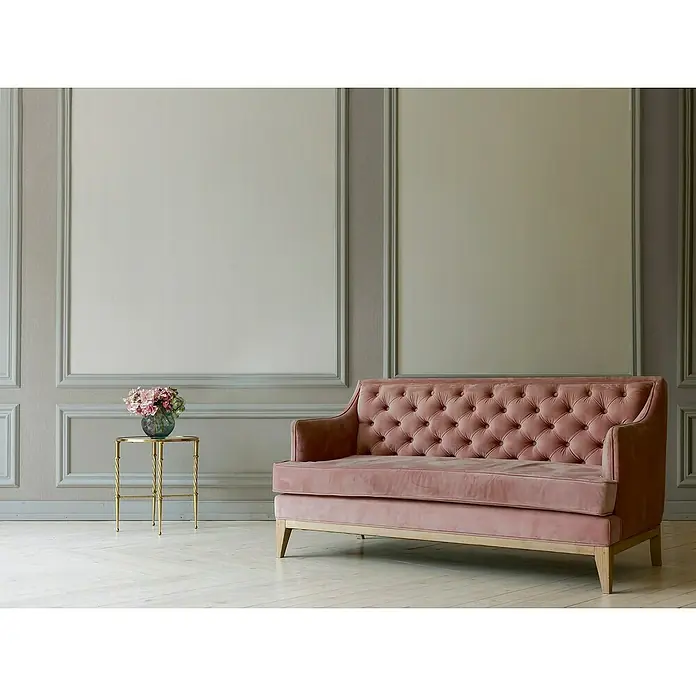 A.S. Création Mata Hari Vliestapete - Cremebeige, Uni, 10,05 x 0,53 m - Elegantes altrosa Samtsofa mit Knopfheftung vor einer stilvollen Wand, ergänzt durch einen goldenen Beistelltisch mit Blumen.
