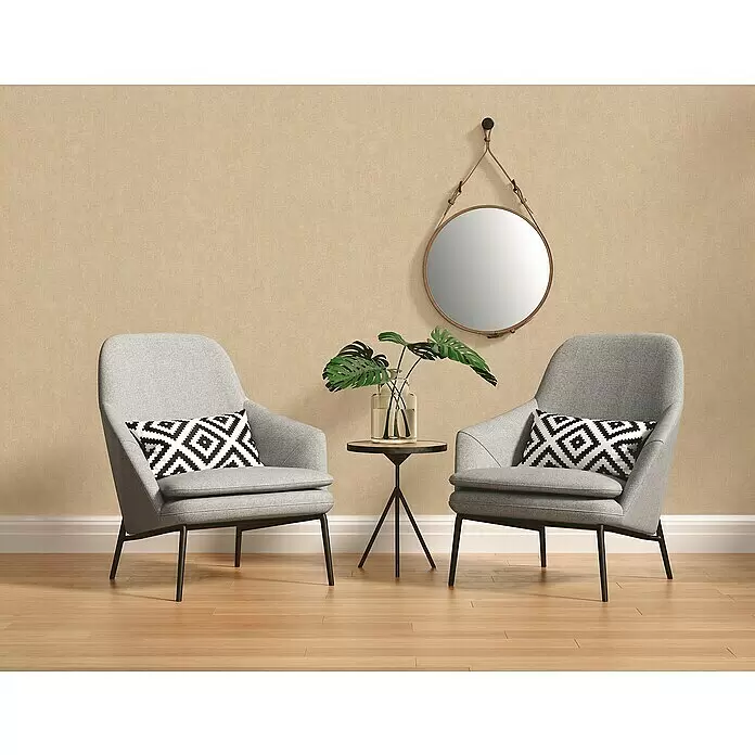 A.S. Création Hygge 2 Vliestapete - Beige, Uni, 10,05 x 0,53 m - Zwei hellgraue Stoff-Sessel mit schwarzen Metallbeinen und gemusterten Kissen flankieren einen Beistelltisch in einem gemütlichen Raum.