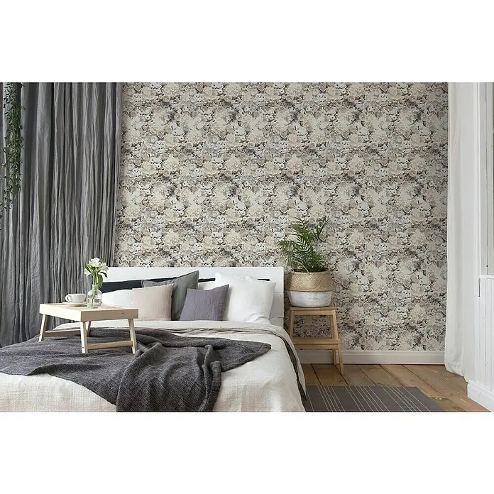 A.S. Création Trendwall 2 Vliestapete Blumen - Grau/Beige, Floral, 10,05 x 0,53 m - Schlafzimmer mit floraler Tapete, hellem Holzboden, weißem Bett mit grauer Decke und Kissen sowie einem Holzhocker mit Pflanze.