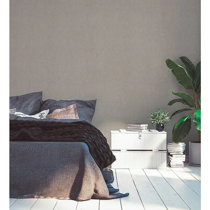 A.S. Création Hygge 2 Vliestapete - Dunkeltaupe, Uni, 10,05 x 0,53 m - Schlafzimmer Interieur mit einem Bett mit grauer Bettwäsche, einem weißen Nachttisch und Zimmerpflanzen, die eine ruhige Atmosphäre schaffen.