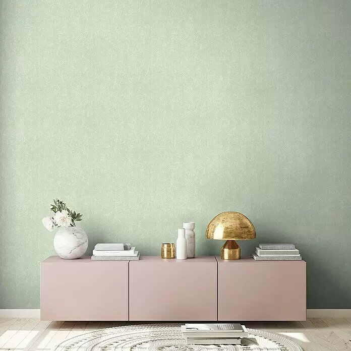 A.S. Création Hygge 2 Vliestapete - Grün/Schwarz, Uni, 10,05 x 0,53 m - Hellgrüne, strukturierte Wandverkleidung in einem modernen Raum, mit rosa Schrank und Dekoration.