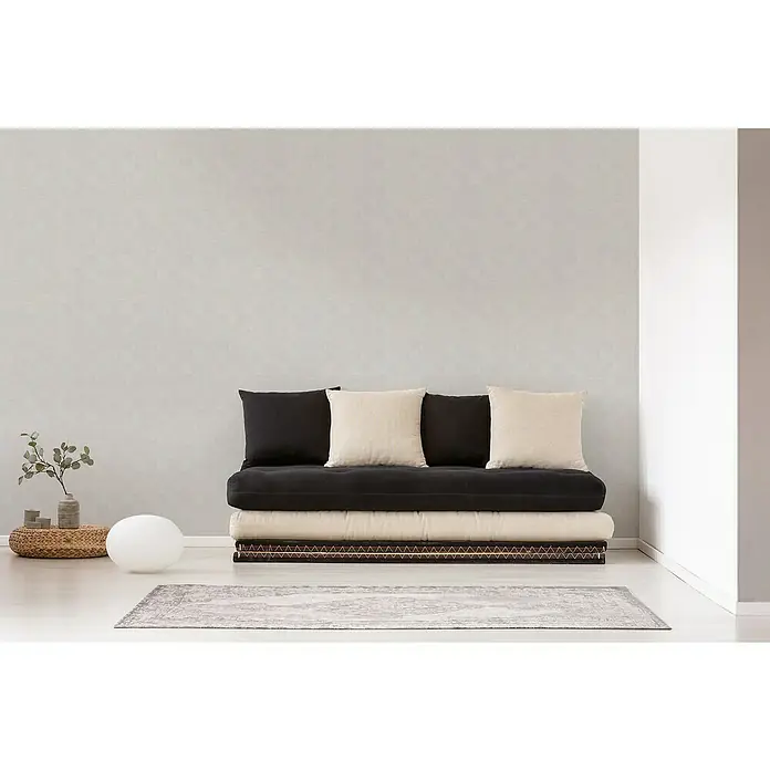 A.S. Création Titanium 3 Vliestapete - Weiß, Grafisch, 10,05 x 0,53 m - Ein stilvolles Futon-Sofa mit schwarzen und beigen Kissen vor einer schlichten Wand, ideal für moderne Wohnräume.