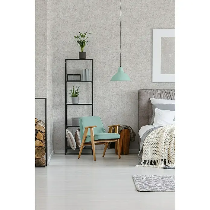 A.S. Création Trendwall 2 Vliestapete - Lebendiges Hellbeige, Uni, 10,05 x 0,53 m - Gemütliche Leseecke mit mintgrünem Sessel, Regal mit Pflanzen und Büchern sowie einem stilvollen Teppich vor einem komfortablen Bett.
