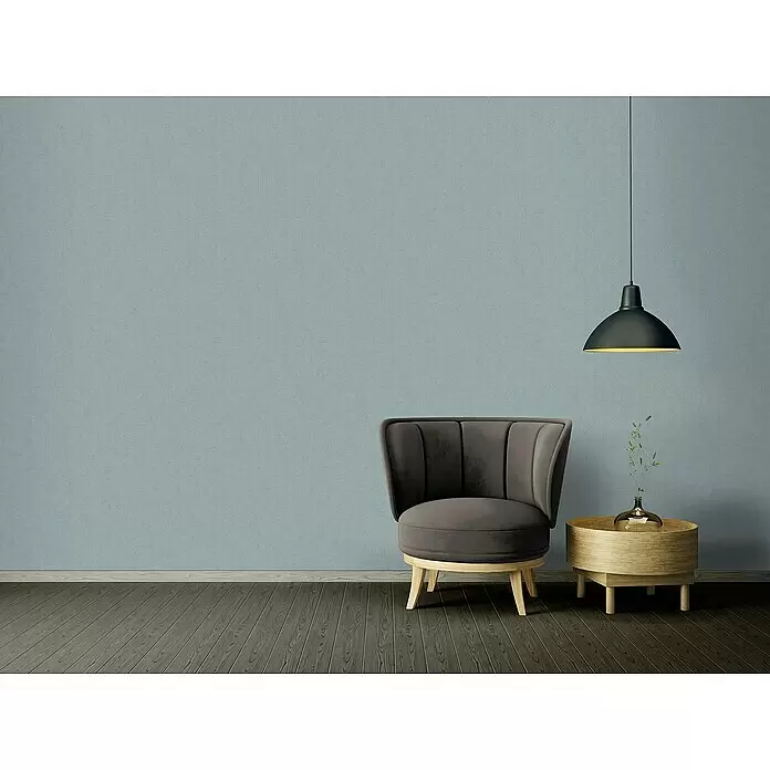 A.S. Création Titanium 3 Vliestapete - Pastellblau, Uni, 10,05 x 0,53 m - Grauer Polstersessel, runder Holznebentisch mit Vase und schwarze Pendelleuchte vor einer blau-grauen Wand.