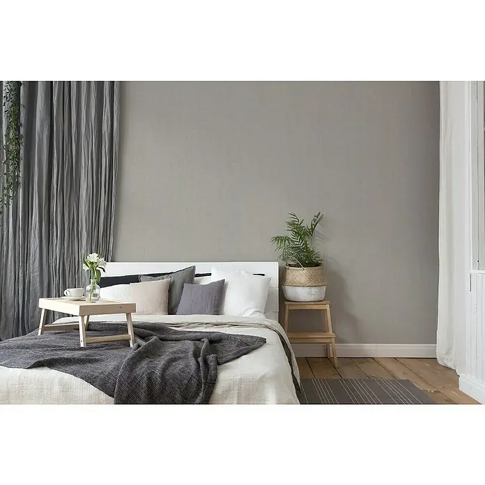 A.S. Création Titanium 3 Vliestapete - Pastellgrau, Uni, 10,05 x 0,53 m - Ein stilvolles Schlafzimmer mit einem komfortablen Bett, das mit Kissen und einer grauen Decke dekoriert ist, für eine entspannte Atmosphäre.