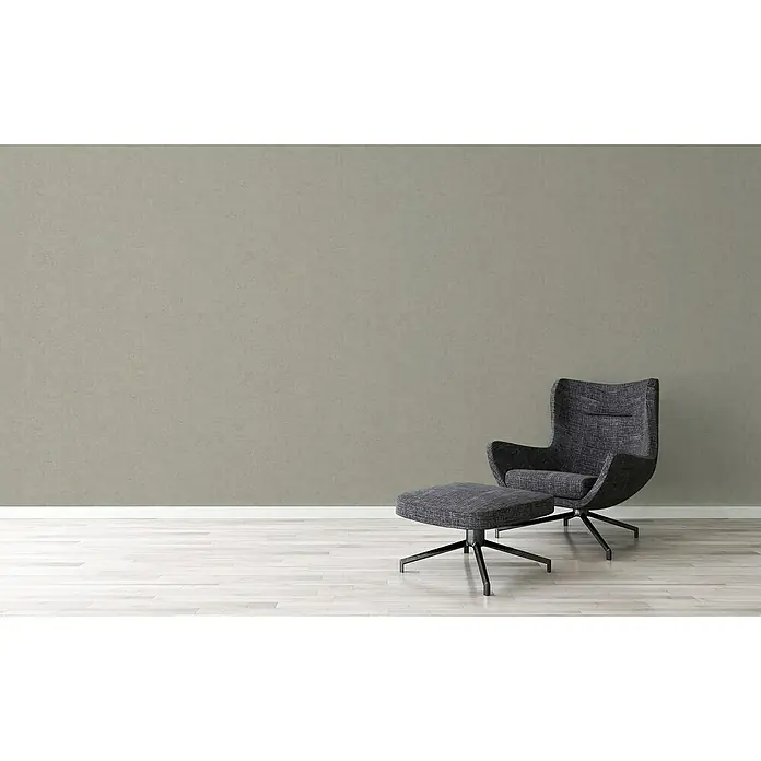A.S. Création Titanium 3 Vliestapete - Pastellgrau, Uni, 10,05 x 0,53 m - Elegante, dunkle Lounge-Sessel- und Ottomane-Kombination vor einer neutralen Wand, die Komfort und stilvolles Design ausstrahlt.
