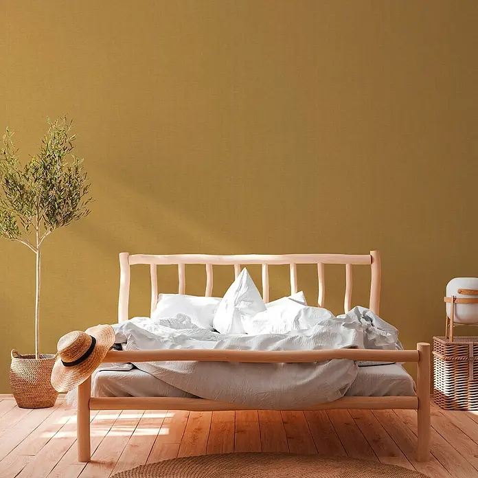 A.S. Création Hygge 2 Vliestapete Gewebe - Gelb/Gold, Uni, 10,05 x 0,53 m - Ein helles Holzbett mit weißer Bettwäsche dominiert den Raum, daneben ein Korb mit Pflanze und ein kleiner Beistelltisch.
