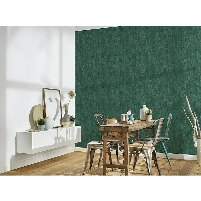 A.S. Création Trendwall 2 Vliestapete Rostoptik - Rost/Grün, Metalloptik, 10,05 x 0,53 m - Esszimmer mit Esstisch und Stühlen vor einer dunkelgrünen Wand, die eine gemütliche Atmosphäre schafft. Das minimalistische Design wird durch Holzböden ergänzt.