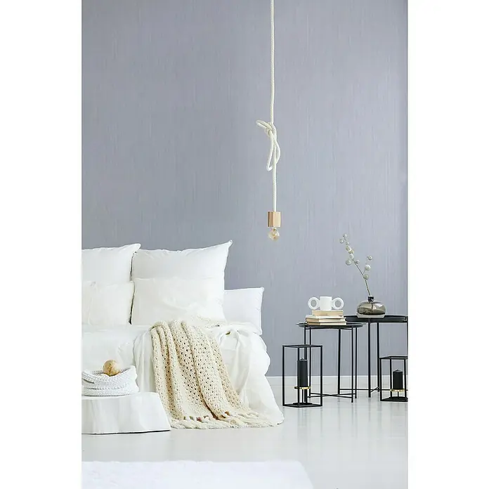 A.S. Création Attractive Vliestapete - Pastellblau, Uni, 10,05 x 0,53 m - Schlafzimmerinterieur mit einem weißen Bett, einer Strickdecke und einem hölzernen Nachttisch mit Dekorationen, die eine friedliche Atmosphäre schaffen.