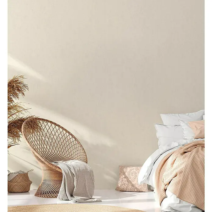 A.S. Création Hygge 2 Vliestapete - Creme, Uni, 10,05 x 0,53 m - Elegantes Schlafzimmer-Interieur mit einem Korbsessel, weichen Textilien und sanften Farben, das eine entspannende Atmosphäre schafft.