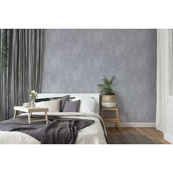 A.S. Création Titanium 3 Vliestapete I - Dunkelgrau, Betonoptik, 10,05 x 0,53 m - Graue, strukturierte Wandverkleidung schafft eine moderne, beruhigende Kulisse in einem Schlafzimmer mit Bett.
