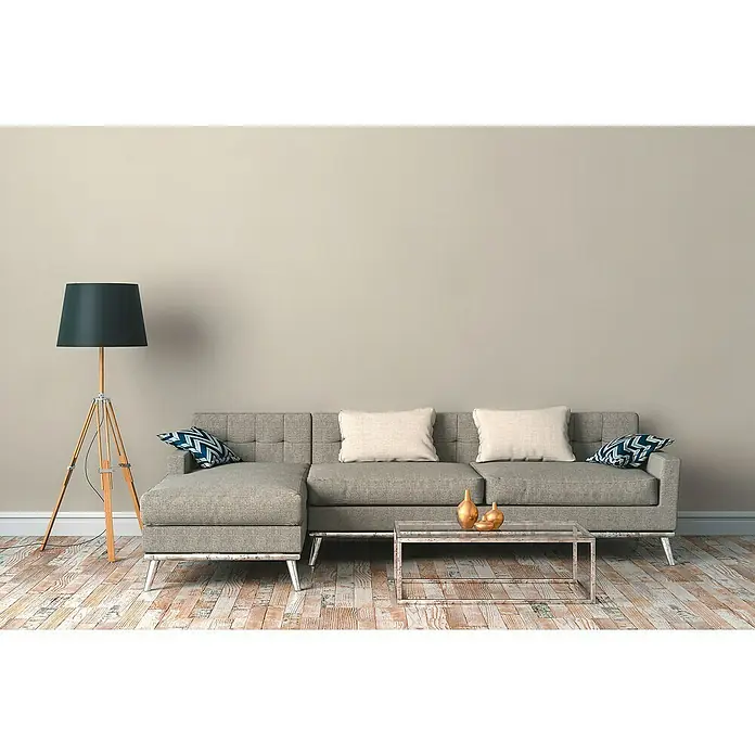 A.S. Création Desert Lodge Vliestapete - Sandgrau, Uni, 10,05 x 0,53 m - Graues Stoffsofa mit Kissen und Beistelltisch vor einer grauen Wand, mit einer eleganten Stehlampe für eine gemütliche Atmosphäre.