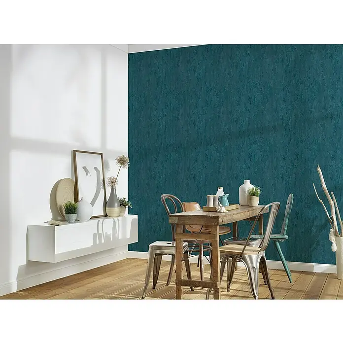 A.S. Création Trendwall 2 Vliestapete Rostoptik - Rost/Blau, Metalloptik, 10,05 x 0,53 m - Dieses Bild zeigt eine moderne Essecke mit einem Holztisch und Stühlen vor einer strukturierten, petrolfarbenen Wand. Auf dem Tisch stehen Deko-Objekte.
